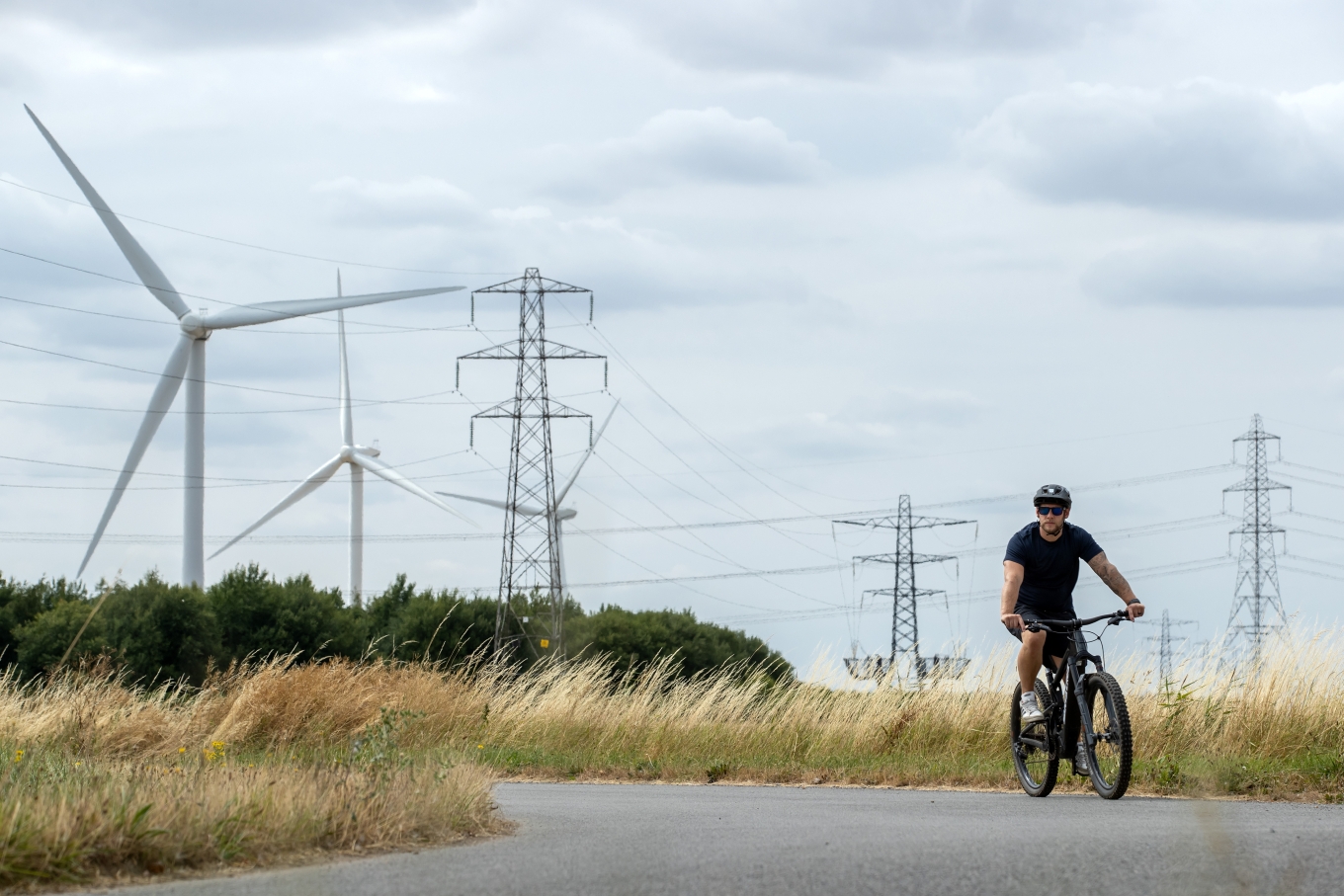 A man riding a bike with pylons and wind turbines in the background